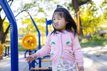 A cute little Asian girl is playing on the playground equipment at Sa Kaeo,asian girl playing in playground,Young girl sitting on yellow playground equipment