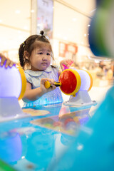 A cute little Asian girl is playing a coin-operated game machine in a shopping mall,Cute little girl adjusting knob and pressing red button while looking at screen of game machine at leisure center