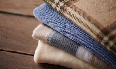 Folded blankets with different textures and patterns stacked on a wooden surface
