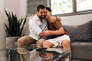 Father and teenage son hugging on a sofa at home, expressing emotional support, trust, and family bonding.