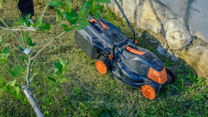 A close-up shot of a lawnmower while a middle-aged man is mowing the grass in his garden