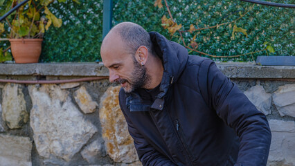 A middle-aged man mowing the grass in his garden with a lawnmower on a winter day