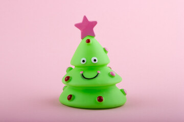 Small green toy Christmas tree with on pink background. Happy New Year concept.