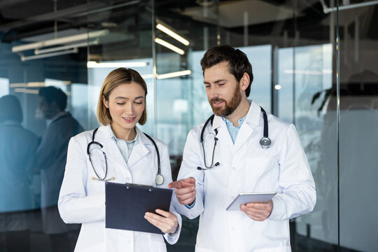 Medical professionals collaborating in a modern clinic, reviewing patient data on a digital tablet and clipboard while discussing diagnosis, treatment options and care plans - Powered by Adobe