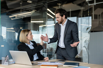 Male and female colleagues in a tense office confrontation, woman gestures stop while man argues,...
