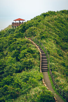 The image of a wooden staircase walkway along the Bitoujiao trail, Taiwan. There is a rest pavilion on a hillside surrounded by lush greenery on both sides of the path. Idea for hiking background.