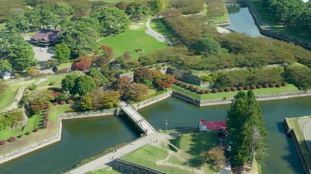 Panoramic aerial footage overlooking the star-shaped Goryokaku Fort park surrounded by moat and dense trees with cityscape and distant mountains from Goryokaku Tower in Hakodate Hokkaido Japan.