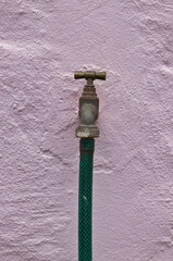 Garden tap with hose on a pink wall.