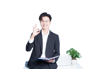 Confident Businessman Gesturing OK Sign: A poised businessman with glasses and a winning smile sits, gesturing the OK sign while holding a notepad, projecting confidence and competence.