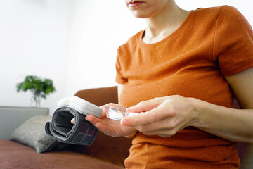 Woman examining medication pills and a blood pressure monitor at home. Symbolizes hypertension management, cardiovascular health monitoring, preventive medicine, and chronic condition control.