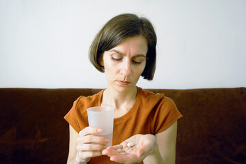 Woman concentrating on pills in her hand with a glass of water for medication intake. Symbolizes...