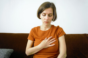 Millennial woman with a hand on her chest. Represents breathlessness assessment, respiratory-cardiovascular link, physical sensation awareness, symptom tracking, and need for medical attention.