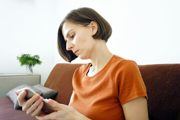 Woman relaxing on a couch while browsing a smartphone screen in a minimalist home interior. Symbolizes digital lifestyle habits, mobile connectivity, indoor leisure time, and technology dependency.