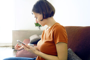 Woman using smartphone for health app and monitoring blood pressure at home. Represents digital health integration, mobile medical tracking, connected care solutions, and modern healthcare convenience