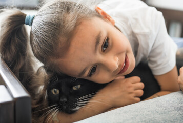 Child gir wearing white clothes hugging cute shorthair cat at home. People taking care of animal concept.