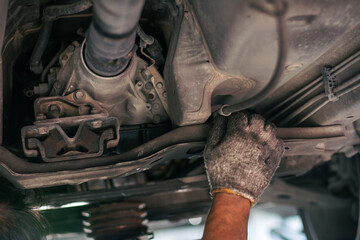 A professional technician checking the transmission housing, rubber mounts, and driveshaft under a vehicle during a routine maintenance inspection.