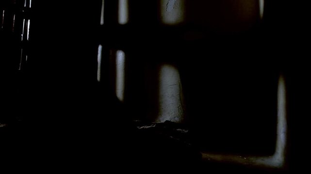 An old prison cell, with the door closing and opening, showing the shadows casting by the door. on the floor there's a dirty rug, a blanket and a black metal bucket. 