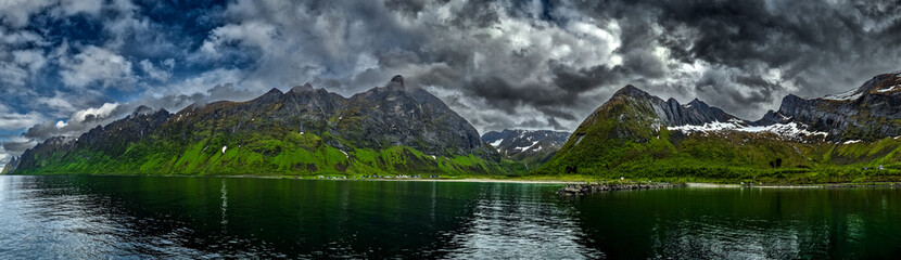 Calm Fjord With Red Huts In Front Of Snowy Mountains On Senja Island In Norway