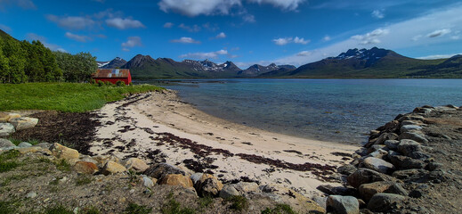 White Sand Beach With Red Hut And Snowy Mountains At Fjord On Lofoten In Norway