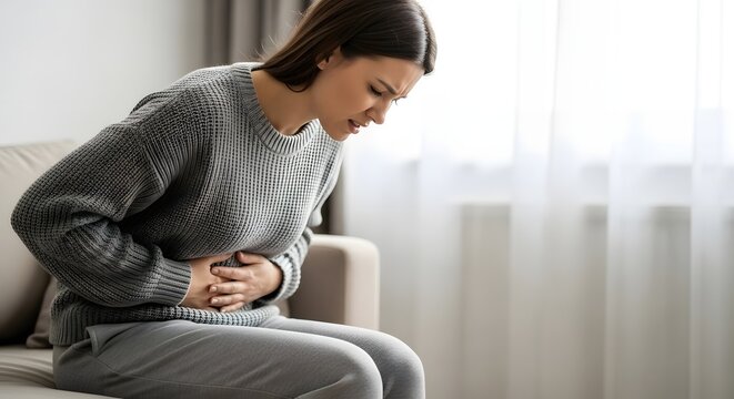 Young woman rubbing her belly in pain, experiencing severe abdominal discomfort at home, illustrating a medical health problem concept.