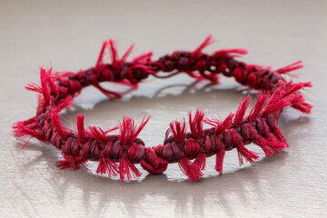 A handmade textile accessory with knotted patterns and decorative red fringe. Close-up on a neutral surface in natural light.