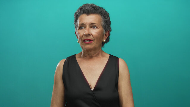 Elderly woman with grey hair wearing black dress against blue background looking directly at camera conveying confidence and dignity in a studio setting