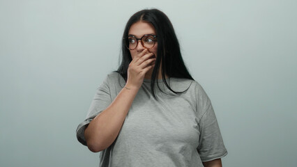 Woman with glasses covers mouth in shock on isolated white background expressing surprise or disbelief in a candid moment with clear emphasis on her expression and natural look.