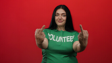Woman volunteer in green shirt showing irreverent gesture on red background conveys attitude and confidence with a playful expression.