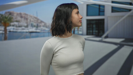 Young hispanic woman face closes eyes while standing upright against modern building exterior with a distant marina behind her  serenity. © Krakenimages.com