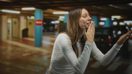 Young hispanic woman blows kiss with hand to lips while reaching out toward camera inside a parking...