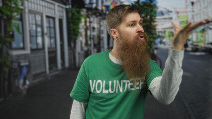 Fototapeta premium Young bearded man blowing kiss on busy city street wearing green volunteer shirt; affection generosity kindness compassion.