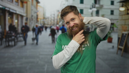 Smiling volunteer man in green shirt uses hand to pull beard on busy sunlit street; compassion...