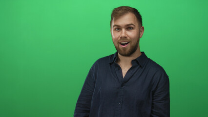 Young caucasian man with beard and open collar looks right and speaks in green studio, profile pose; surprise.