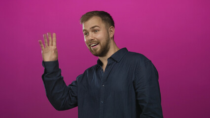 Naklejka premium Man waving right hand in studio wearing navy shirt against vibrant pink studio wall; friendly greeting.