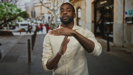 Man in beige linen shirt gesturing with hands and looking down while standing on a busy city...