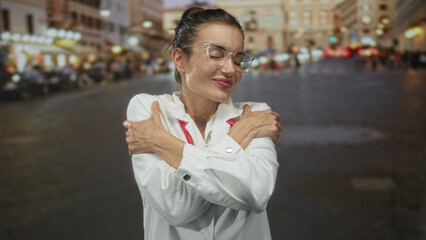 Fototapeta premium Young hispanic woman doctor adjusts stethoscope and smiles on city street under glowing lights; compassion wellness.