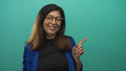 Woman finger raised in call me gesture and pointing finger to the side in teal studio; friendly invitation.