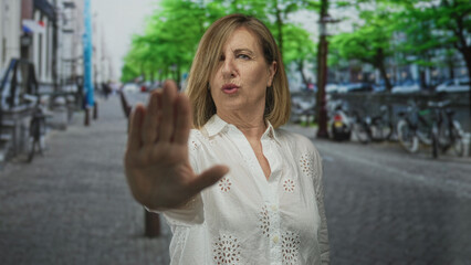 Woman holds hand palm forward in a stop gesture on an urban street lined with parked bicycles against building facades; defiance.