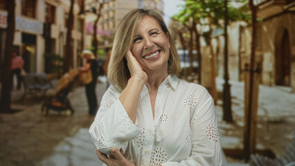 Fototapeta premium Caucasian woman smiling with hand on cheek on old town cobblestone street under warm sunlight; serenity.
