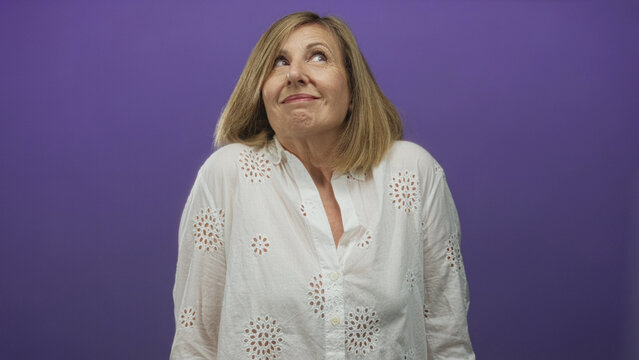 Woman wearing white eyelet blouse tilts face upward with shoulders shrugged in a purple studio; uncertainty.