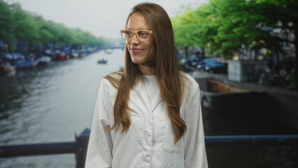 Woman scientist smiling with glasses on a street canal bridge wearing lab coat, eyes closed; science curiosity contentment.