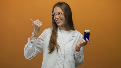 Woman scientist in lab coat holding blue bottle and giving thumbs up in orange studio; confidence wellness trust.