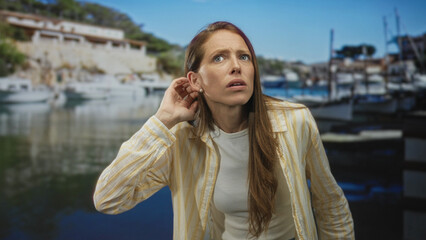 Woman with hand to ear and raised fist in studio port marina set with anchored boats and wooden dock  confusion. © Krakenimages.com