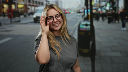 Fototapeta premium Woman smiling on a city street with blonde hair and glasses, enjoying an outdoor urban scene amid a vibrant backdrop.