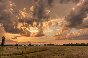 Sunset over a tranquil meadow with dramatic clouds and golden light illuminating the horizon