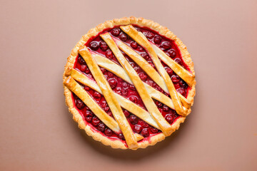 Freshly baked fruit pie with a golden pastry crust and a red berry filling. Top view, symmetrical stripes of pastry on a flat, warm surface.