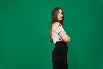 portrait of a beautiful, happy, neat woman in a beige turtleneck sweater and black-rimmed glasses, standing on a light background sideways to the camera and crossing her arms over her chest. photo