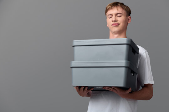 Man holding stacked grey boxes for delivery and storage, illustrating packaging, logistics and inventory in a clean studio setup with focus on workflow and order fulfillment - Powered by Adobe
