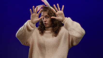 Young woman with curly hair wearing bunny ears gesturing with hands over isolated blue background