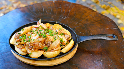 Baked potato with mushrooms and herbs in iron cast pan on wooden table. High quality photo